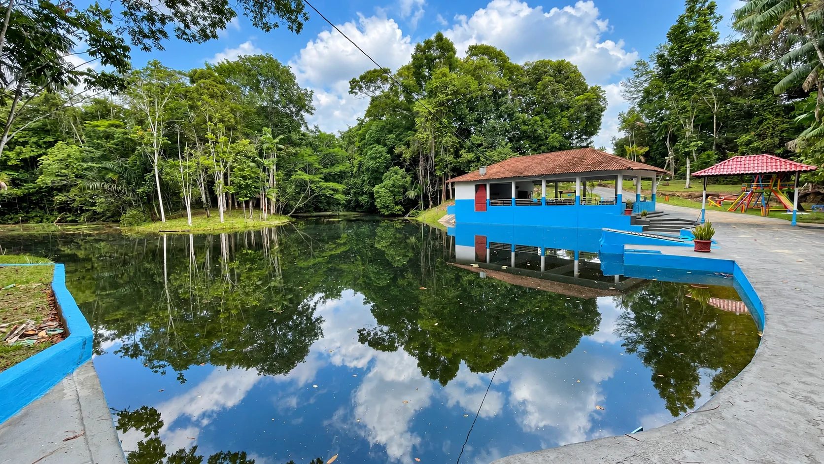 Árvores e céu refletidos na água ao lado do salão do Recanto